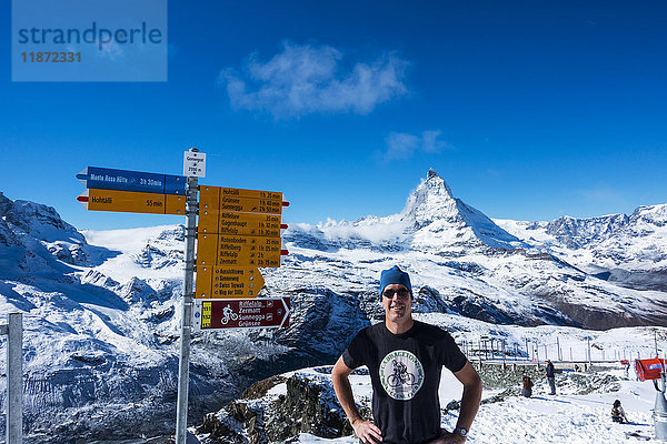 Ein männlicher Tourist posiert vor dem Hotel und Observatorium Gornergrat Kulm mit dem Matterhorn im Hintergrund; Schweiz'.