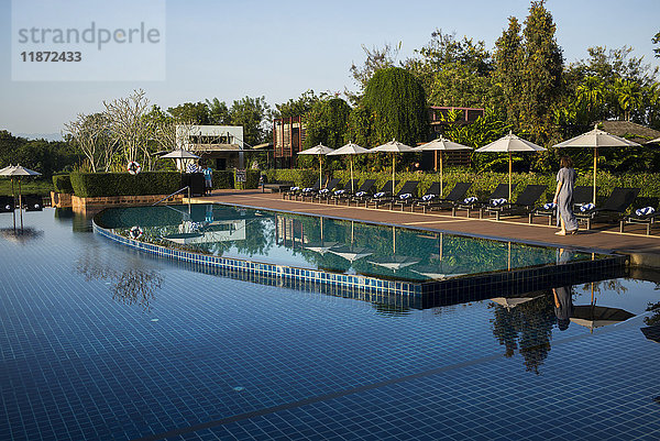 Das ruhige Wasser eines Swimmingpools in einem Resort mit Liegestühlen und Sonnenschirmen; Chiang Rai  Thailand'.
