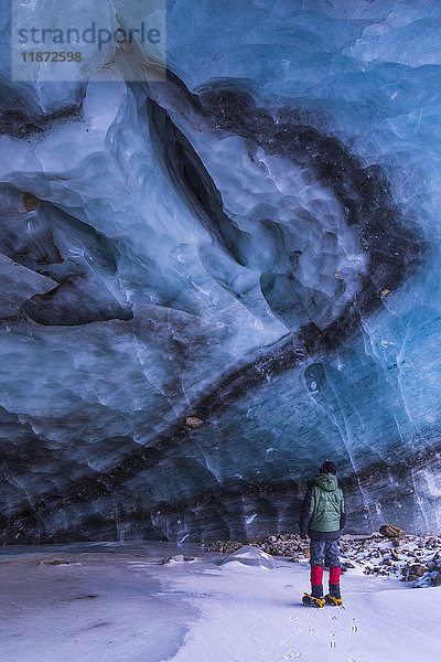 Ein Mann beobachtet einen Riss in der Decke einer Eishöhle im Augustana-Gletscher in der Alaska Range im Winter  Innenalaska  USA.