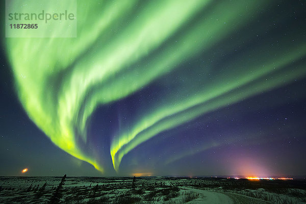 Aurora borealis füllt den Himmel über einer untergehenden Mondsichel und den Lichtern von Fort Greely im Inneren Alaskas  USA.