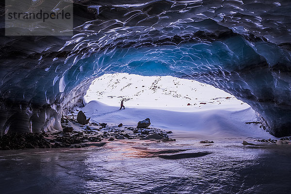 Ein Mann wird vom Eingang einer großen Eishöhle in der Nähe des Endes des Augustana-Gletschers in der Alaska Range im Winter eingerahmt; Alaska  Vereinigte Staaten von Amerika'.