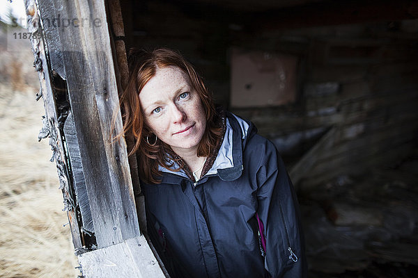 Porträt einer Frau mit roten Haaren  die an einer Holzwand lehnt und in die Kamera schaut; Alaska  Vereinigte Staaten von Amerika'.