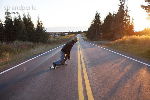 Ein junger Mann fährt in der Abenddämmerung mit dem Skateboard eine Straße entlang; Homer  Alaska  Vereinigte Staaten von Amerika'.