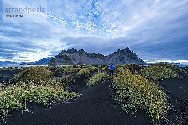 Person auf einem schwarzen Sandhügel mit Blick auf das Vestrahorn oder Stokknes an der Südküste Islands; Hofn  Island'.