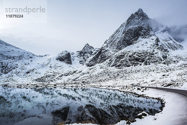 Schneelandschaft mit zerklüfteten Bergen  die sich im ruhigen Wasser spiegeln; Lofoten-Inseln  Nordland  Norwegen'.