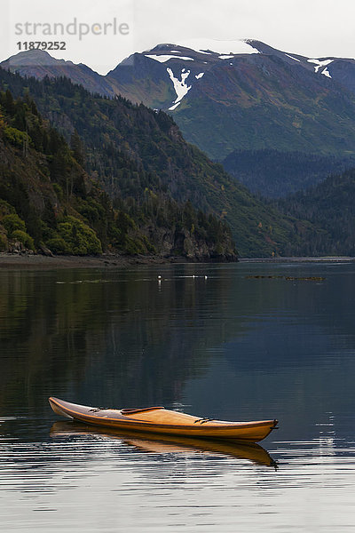 Ein Kajak sitzt auf dem ruhigen Wasser mit Blick auf Wälder und eine Bergkette im Hintergrund  Kachemak Bay State Park; Alaska  Vereinigte Staaten von Amerika'.