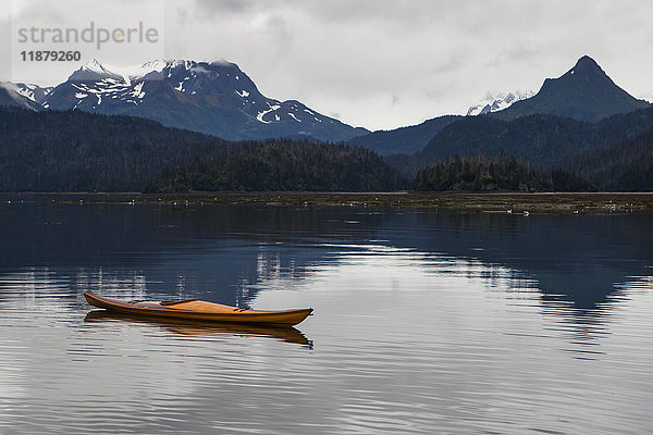Ein Kajak sitzt auf dem ruhigen Wasser mit Blick auf Wälder und eine Bergkette im Hintergrund  Kachemak Bay State Park; Alaska  Vereinigte Staaten von Amerika'.