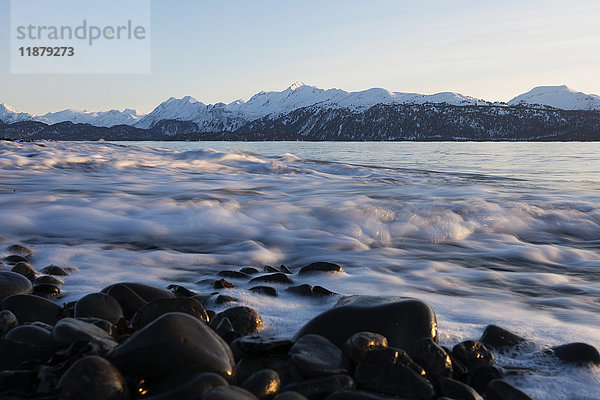 Die Brandung rollt gegen Felsen an der Küste mit schneebedeckter Bergkette im Hintergrund; Alaska  Vereinigte Staaten von Amerika'.