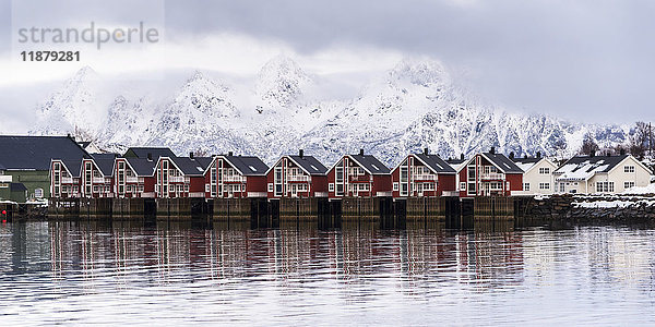 Rote Gebäude am Wasser mit schneebedeckten Bergen im Hintergrund; Svolvar  Lofoten-Inseln  Nordland  Norwegen'.