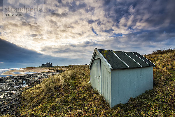 Ein kleiner grüner Schuppen im Gras entlang der Küste mit Bamburgh Castle in der Ferne; Bamburgh  Northumberland  England'.