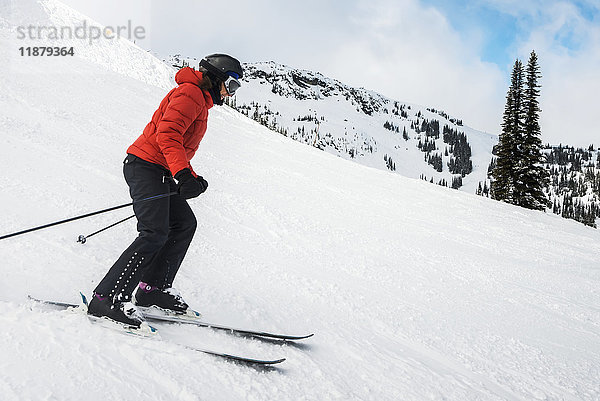 Ein Skifahrer in einem roten Mantel fährt in den schneebedeckten Rocky Mountains; Whistler  British Columbia  Kanada'.