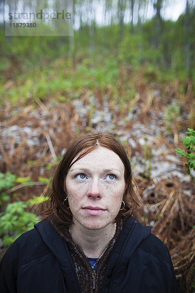 Eine Frau mit roten Haaren blickt in den Himmel mit einem Wald im Hintergrund; Alaska  Vereinigte Staaten von Amerika'.