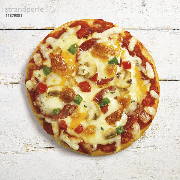 Eine Pizza mit geschmolzenem Käse  Paprika und Pilzen auf einer weißen Holzunterlage