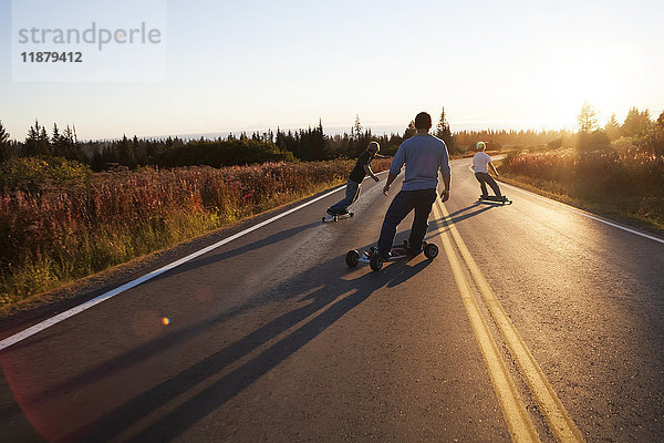 Drei junge Männer fahren bei Sonnenuntergang mit dem Skateboard eine Straße entlang; Homer  Alaska  Vereinigte Staaten von Amerika'.