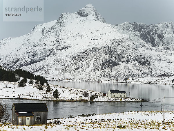 Schroffe  spitze  schneebedeckte Berge und ruhiges Wasser entlang der Küste; Lofoten  Nordland  Norwegen'.