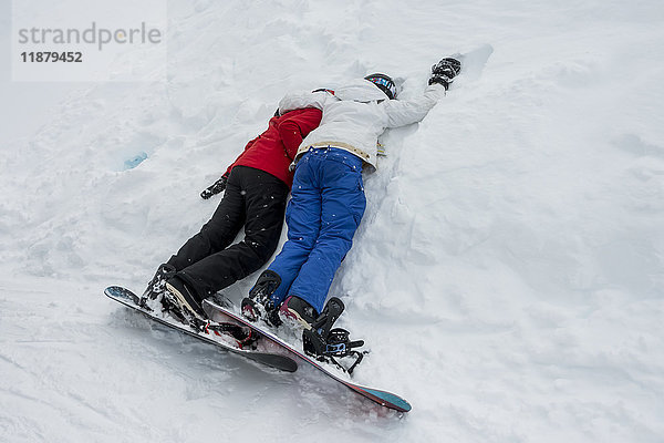 Zwei junge Snowboarder liegen zusammen im Schnee; Whistler  British Columbia  Kanada'.