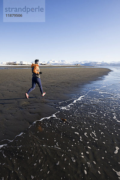 Eine junge Frau joggt am nassen Strand am Rande des Wassers; Homer  Alaska  Vereinigte Staaten von Amerika'.