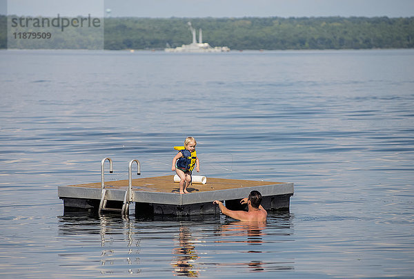 Ein junges kaukasisches Mädchen bereitet sich darauf vor  von einem schwimmenden Steg in die Arme ihres Vaters im Seneca Lake im Bundesstaat New York zu springen; im Hintergrund ist der nicht mehr in Betrieb befindliche Marinekahn zu sehen; Dresden  New York  Vereinigte Staaten von Amerika'.