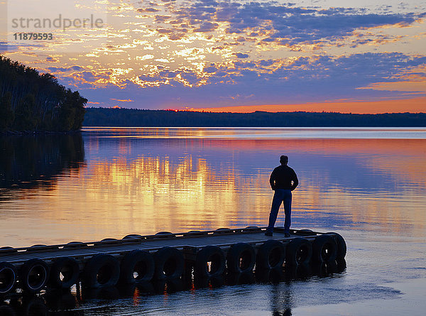 Silhouette einer Person  die am Ende eines Stegs steht und auf einen ruhigen See bei Sonnenuntergang blickt  Gregoire Lake Provincial Park; Alberta  Kanada'.