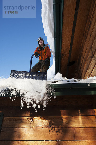 Eine junge Frau entfernt den Schnee vom Dach ihres Hauses; Homer  Alaska  Vereinigte Staaten von Amerika'.