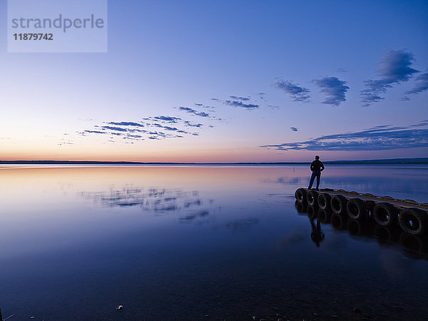 Silhouette einer Person  die am Ende eines Stegs steht und auf einen ruhigen See bei Sonnenuntergang blickt  Gregoire Lake Provincial Park; Alberta  Kanada'.