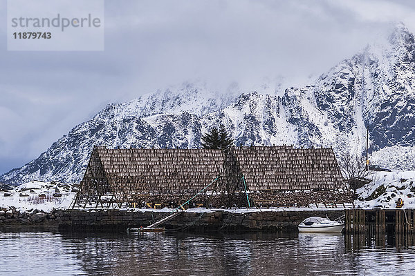 Ein spitz zulaufendes Gebäude am Ufer  das Schutz für die Ausrüstung bietet  mit einem im Wasser vertäuten Boot; Svolvar  Lofoten  Nordland  Norwegen'.