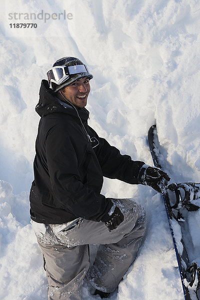 Ein Snowboarder posiert beim Klettern in steilem Gelände im Tiefschnee mit seinem Snowboard; Alaska  Vereinigte Staaten von Amerika'.