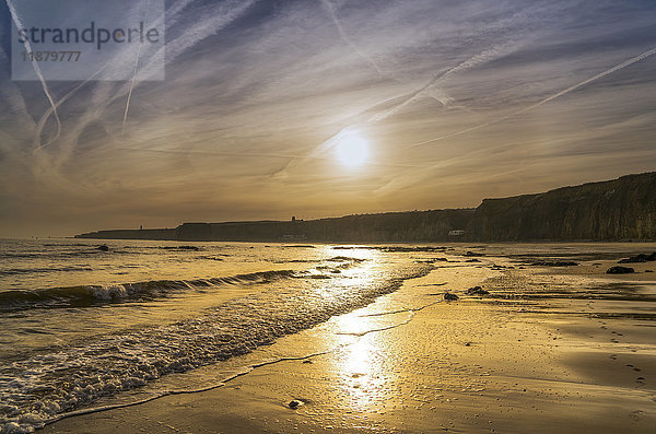 Die untergehende Sonne leuchtet am Himmel und spiegelt sich auf dem nassen Sand entlang der Küste; South Shields  Tyne and Wear  England