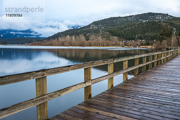 Ein Holzsteg entlang eines ruhigen Sees mit Bergen am Ufer; Whistler  British Columbia  Kanada