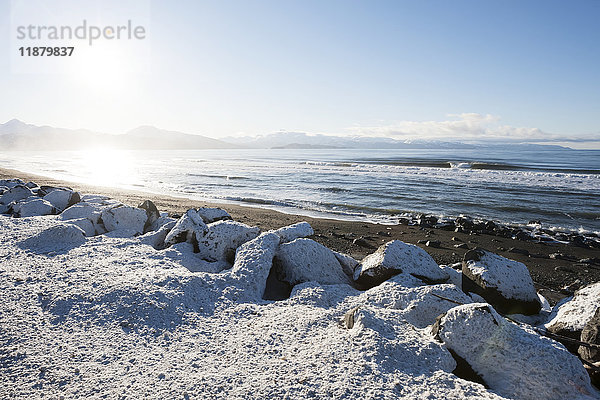 Schneebedeckte Felsen und Strand mit Blick auf den Ozean und die Berge entlang der Küstenlinie; Alaska  Vereinigte Staaten von Amerika