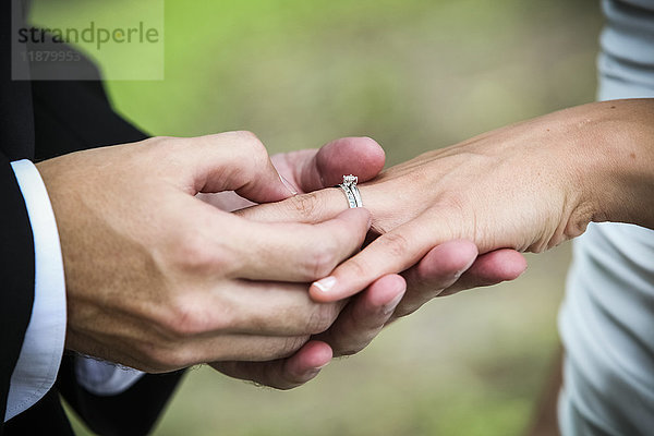 Ein Bräutigam steckt seiner Braut während einer Hochzeitszeremonie einen Ring an den Finger; Ontario  Kanada'.