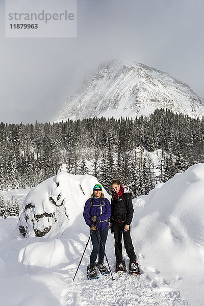 Zwei Schneeschuhläuferinnen auf einem verschneiten Weg mit einem schneebedeckten Berg im Hintergrund; Kananaskis Country  Alberta  Kanada'.