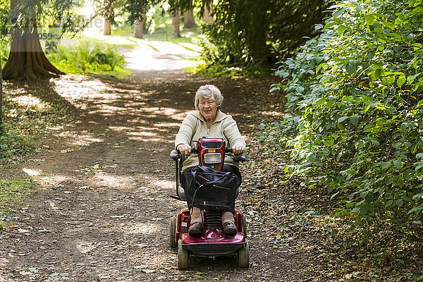 Eine ältere Frau fährt mit einem motorisierten Rollstuhl einen Weg in einem Park hinunter; Yorkshire  England'.