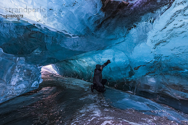 Ein Mann untersucht das klare blaue Eis in einem Tunnel unter der Oberfläche des Black Rapids Glacier im Winter; Alaska  Vereinigte Staaten von Amerika'.