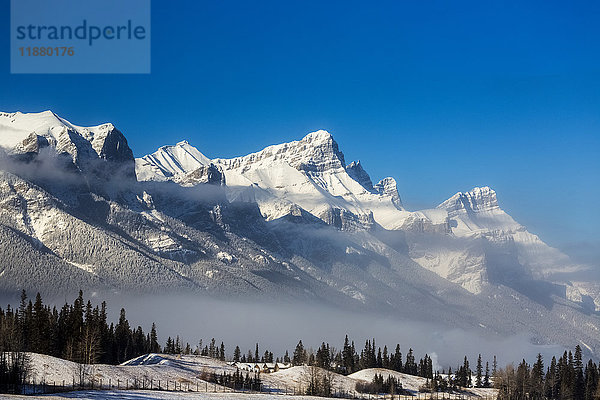 Schneebedeckte Bergkette mit Wolken im Tal  vereiste Bäume und blauer Himmel; Canmore  Alberta  Kanada'.