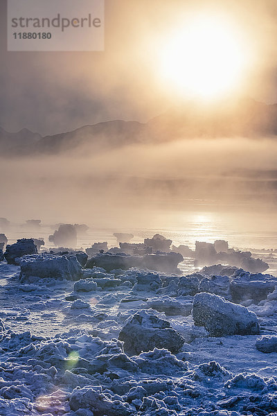 Niedriger Nebel im warmen Licht des Sonnenuntergangs entlang des Turnagain Arm und des Seward Highway im Winter  das Meereis bedeckt den Ozean im Vordergrund  die Chugach Moutains sind im Hintergrund zu erkennen  Süd-Zentral-Alaska; Alaska  Vereinigte Staaten von Amerika'.