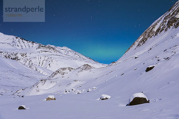 Ein sehr schwaches Band von Polarlichtern erstreckt sich zwischen den Bergen an einem abgelegenen Ort in der Alaska Range im Winter  in der Nähe des Augustana Glacier; Alaska  Vereinigte Staaten von Amerika'.