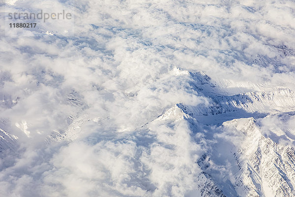 Luftaufnahme eines schneebedeckten Berggipfels  der sich über tief hängenden Wolken in der Denali-Gebirgskette erhebt  die Sonne wirft Schatten in die niedrigen Täler darunter  Süd-Zentral-Alaska; Alaska  Vereinigte Staaten von Amerika'.