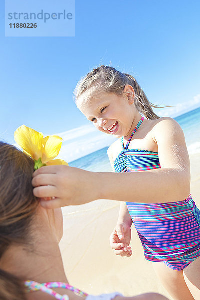 Ein junges Mädchen steckt ihrer Mutter am Strand eine tropische Blume ins Haar; Hawaii  Vereinigte Staaten von Amerika'.