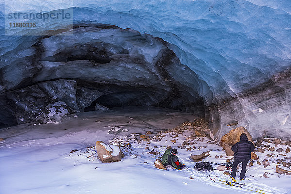 Zwei Männer packen ihre Ausrüstung zusammen  nachdem sie eine Eishöhle des Augustana-Gletschers im Winter erkundet haben; Alaska  Vereinigte Staaten von Amerika'.