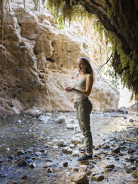 Eine junge Frau steht auf einem Felsen entlang eines Baches in der Dodim-Höhle  Naturreservat Ein Gedi; Süddistrikt  Israel'.