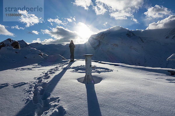 Eine Frau steht bei Sonnenaufgang im Schnee auf dem Gornergrat-Gipfel  Monte Rosa  Penninische Alpen; Zermatt  Wallis  Schweiz'.