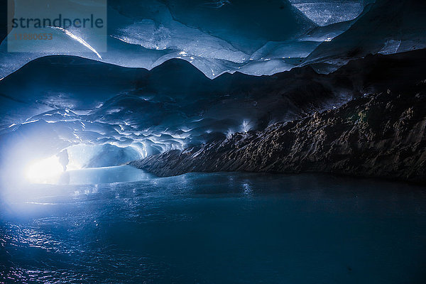 Ein Mann steht als Silhouette vor dem Eingang einer dunklen Eishöhle im Augustana-Gletscher in der Alaska Range; Alaska  Vereinigte Staaten von Amerika'.