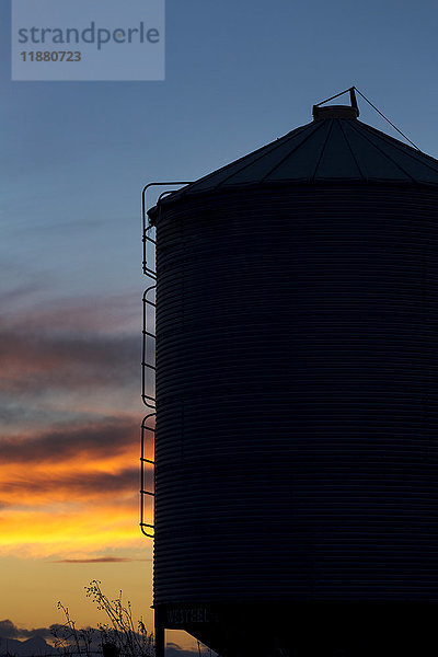 Silhouette eines großen Getreidesilos aus Metall mit bunten Wolken bei Sonnenuntergang und blauem Himmel; Alberta  Kanada'.