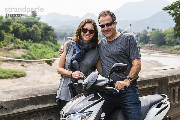 Ein Paar posiert neben einem Motorrad vor einer Berglandschaft in der Ferne; Luang Prabang  Provinz Luang Prabang  Laos'.