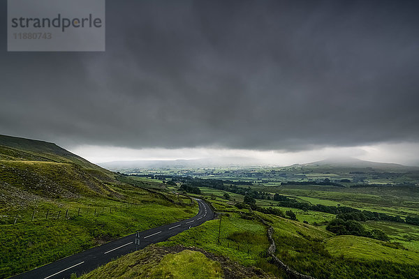 Dunkle Gewitterwolken über einer üppigen  grünen Landschaft und einer Straße; North Yorkshire  England'.