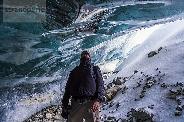 Ein Mann blickt auf das Eis des Canwell-Gletschers  während er im Eingang einer Eishöhle steht; Alaska  Vereinigte Staaten von Amerika'.