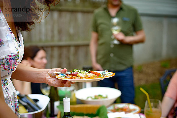 Frau auf Gartenparty  die einen Teller mit Essen hält  Mittelteil