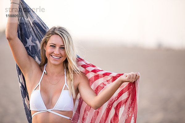 Porträt einer jungen Frau im Bikini-Oberteil  die die amerikanische Flagge hochhält  Santa Monica  Kalifornien  USA