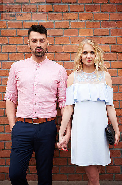 Porträt eines Paares  das sich vor einer Ziegelmauer an den Händen hält